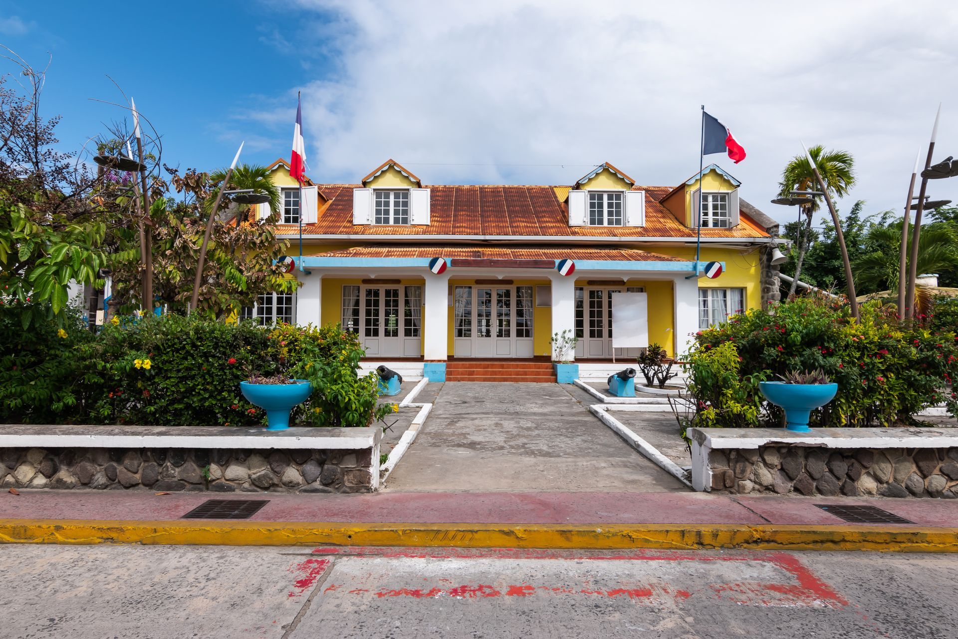 Maison jaune symétrique au toit de tuiles rouges, marches d'entrée et drapeaux vietnamiens sous un ciel bleu