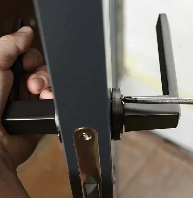 Una persona está arreglando la manija de una puerta con un destornillador.