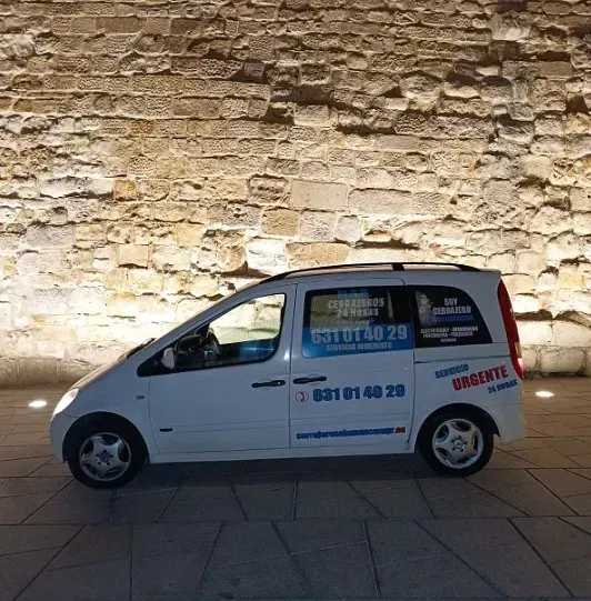 Una furgoneta blanca está aparcada delante de un muro de piedra.