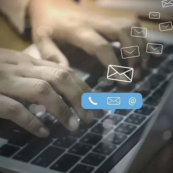 Una persona está escribiendo en una computadora portátil con íconos de sobres que salen del teclado.