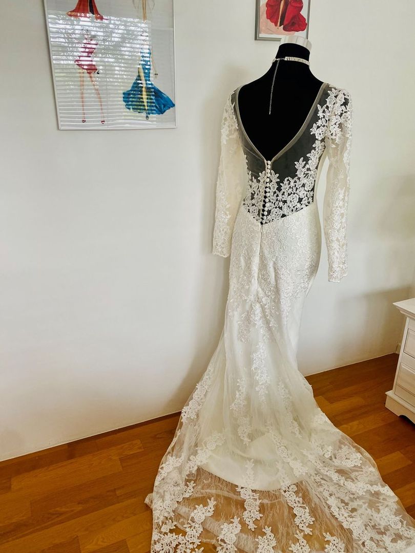In einem Raum hängt auf einer Schaufensterpuppe ein weißes Brautkleid aus Spitze.