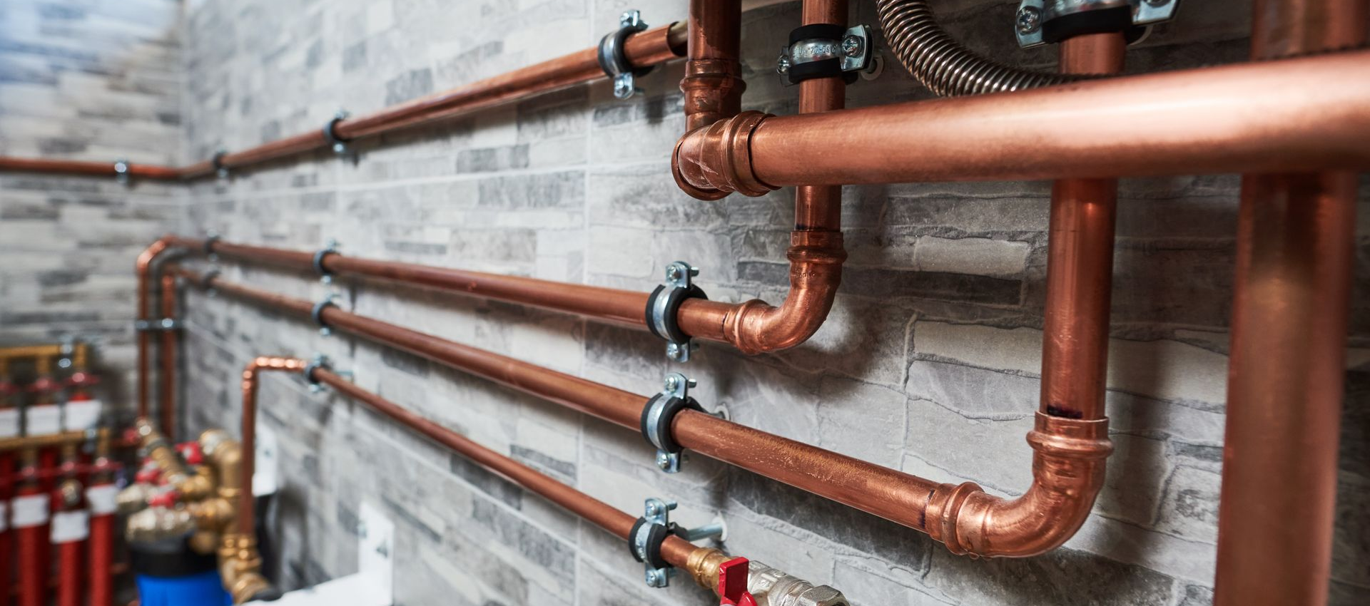 Tuyaux de cuivre installés sur un mur de briques grises.