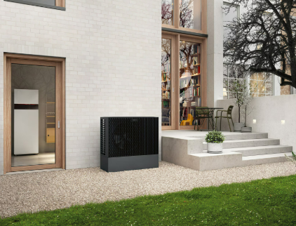 Unité de climatisation blanche fixée sur un mur de briques, à côté d'une pelouse verte et d'un jardin.