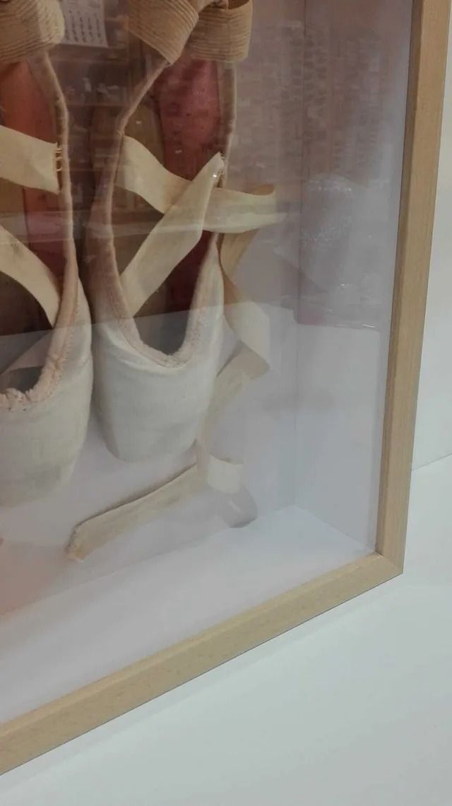 Un par de zapatillas de ballet en un marco de cristal sobre una mesa.