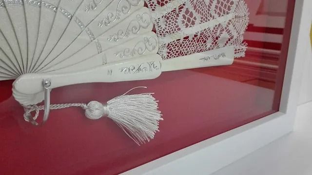 Un abanico blanco con una borla está en un marco blanco.