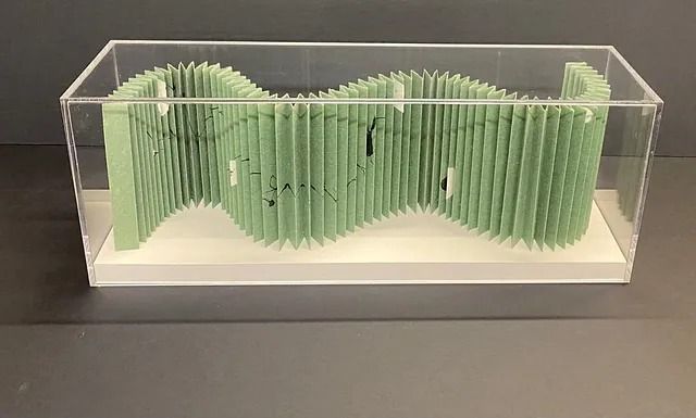 Una escultura verde está sentada en una caja transparente sobre una mesa.