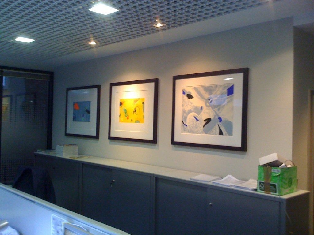 Tres cuadros enmarcados están colgados en una pared en una oficina.