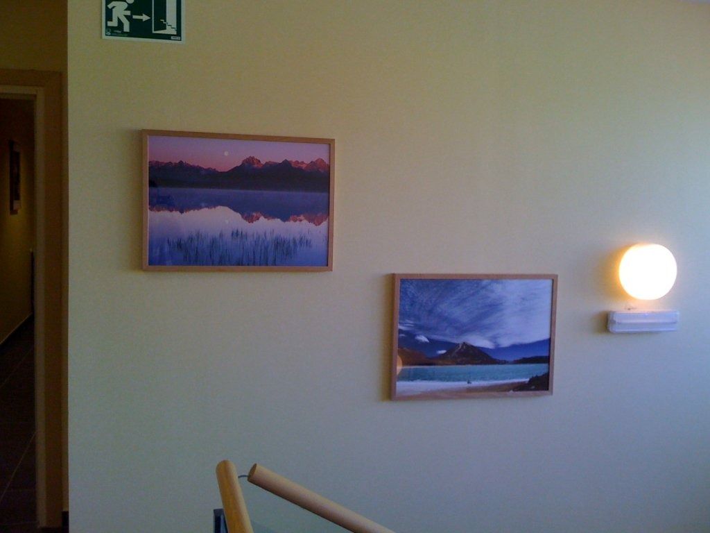 Una señal de salida verde cuelga sobre dos cuadros enmarcados en una pared.