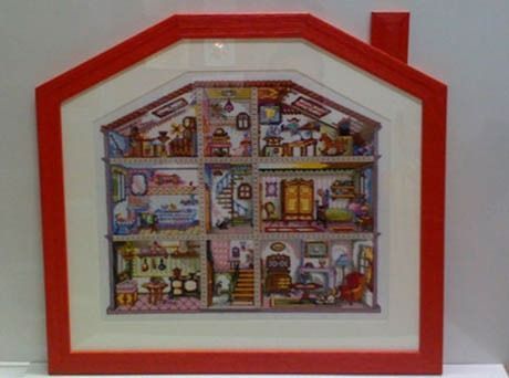 Un punto de cruz de una casa de muñecas en un marco rojo.