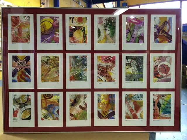 Una exposición de pinturas en una pared con un marco rojo.