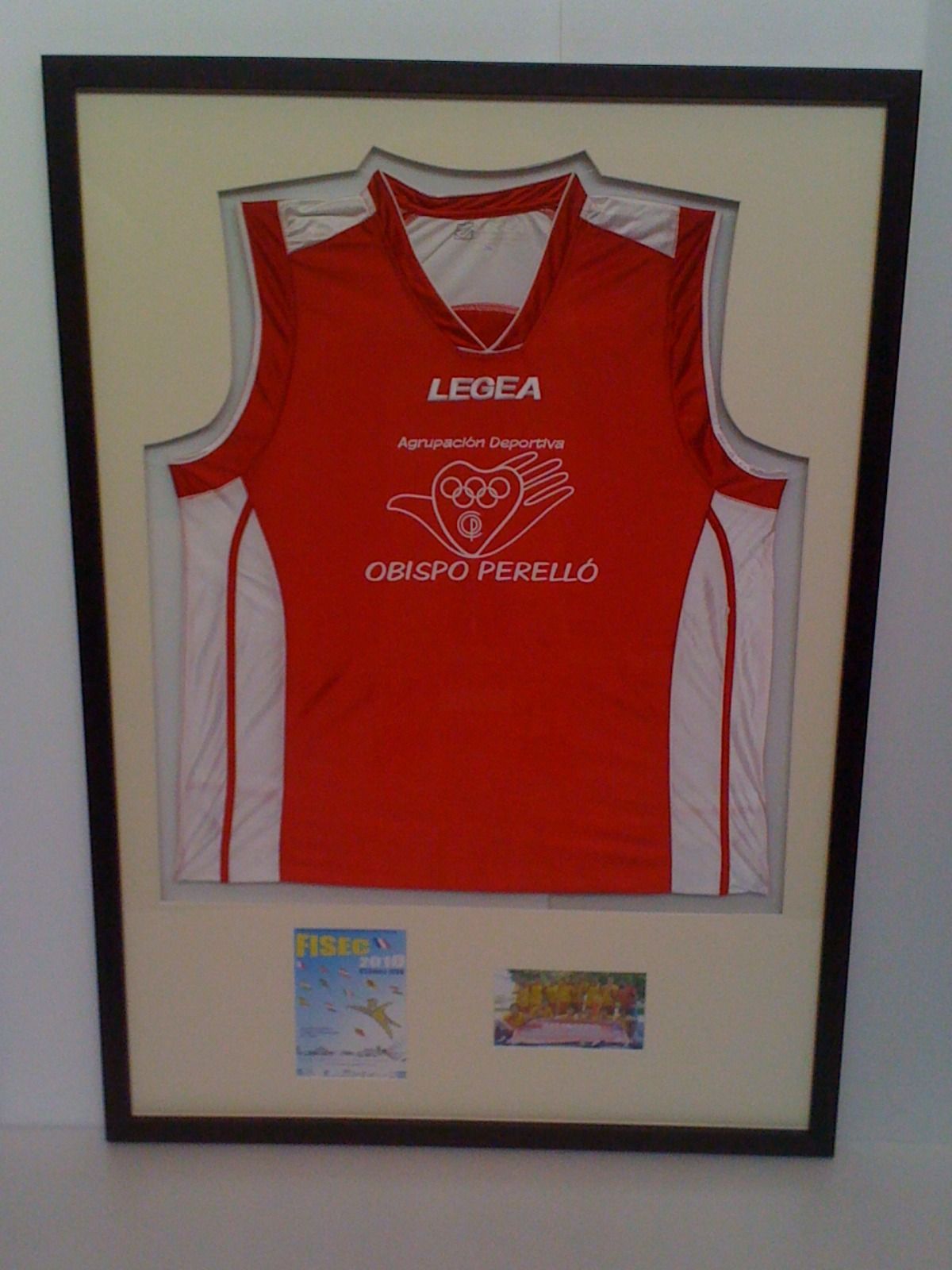 Una camiseta roja de Legea está enmarcada en una pared blanca