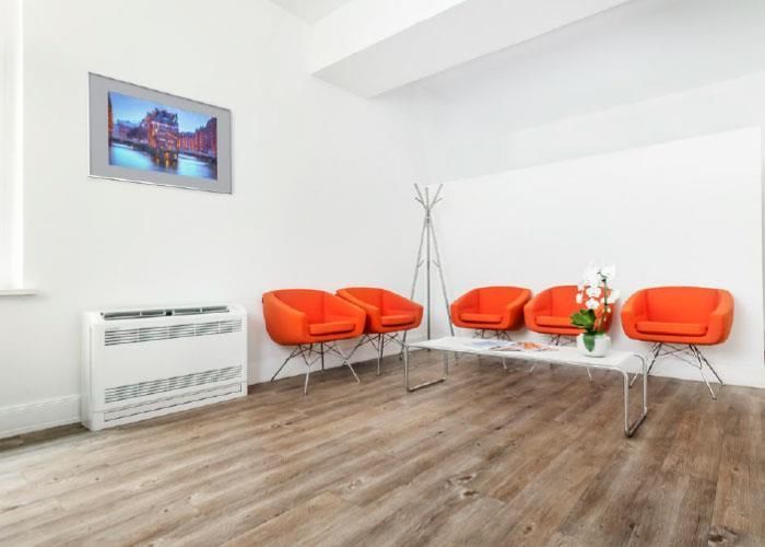 Ein Wartezimmer mit orangefarbenen Stühlen und einem Fernseher an der Wand.