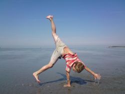 Ein kleiner Junge macht am Strand einen Handstand.