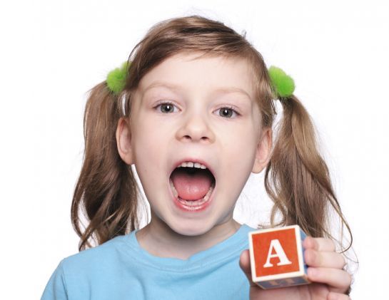 Ein kleines Mädchen hält einen Bauklotz mit dem Buchstaben A darauf.