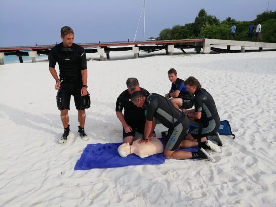 Eine Gruppe von Menschen übt eine Herz-Lungen-Wiederbelebung an einem Sandstrand