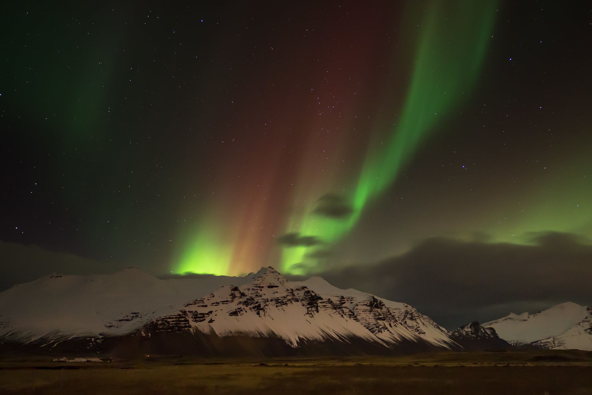 Green and red aurora borealis over snow-covered mountains at night.