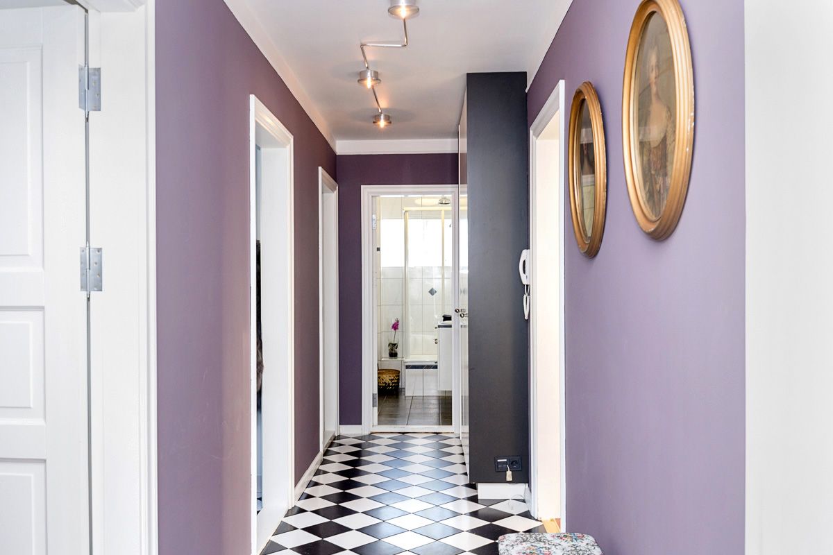 Purple hallway with black and white tiled floor, two oval paintings, and a dark gray accent wall.