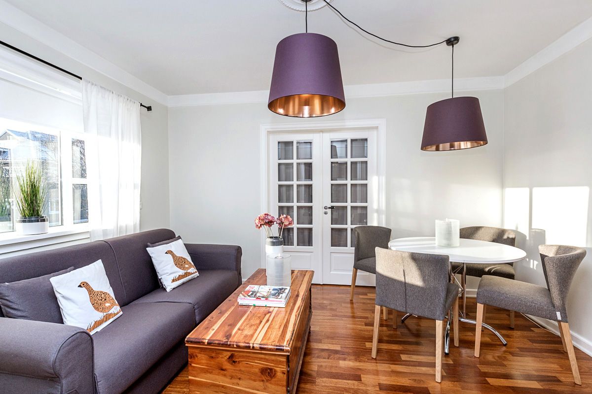 Living room: purple sofa, round table, chairs, plum-colored lamps, wooden trunk, white walls, and wooden floors.