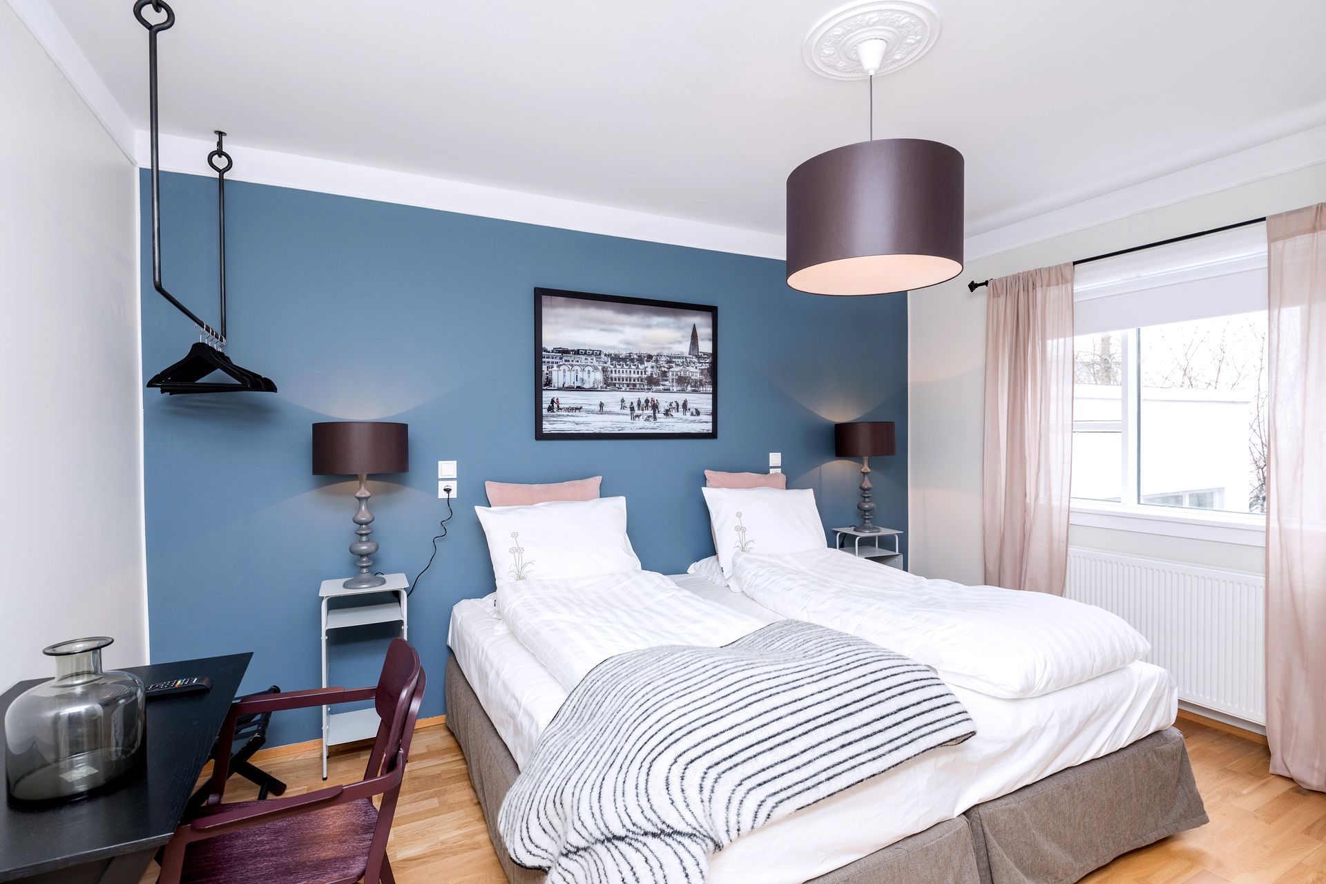 Blue-walled hotel room with two beds, a desk, and a window with curtains.