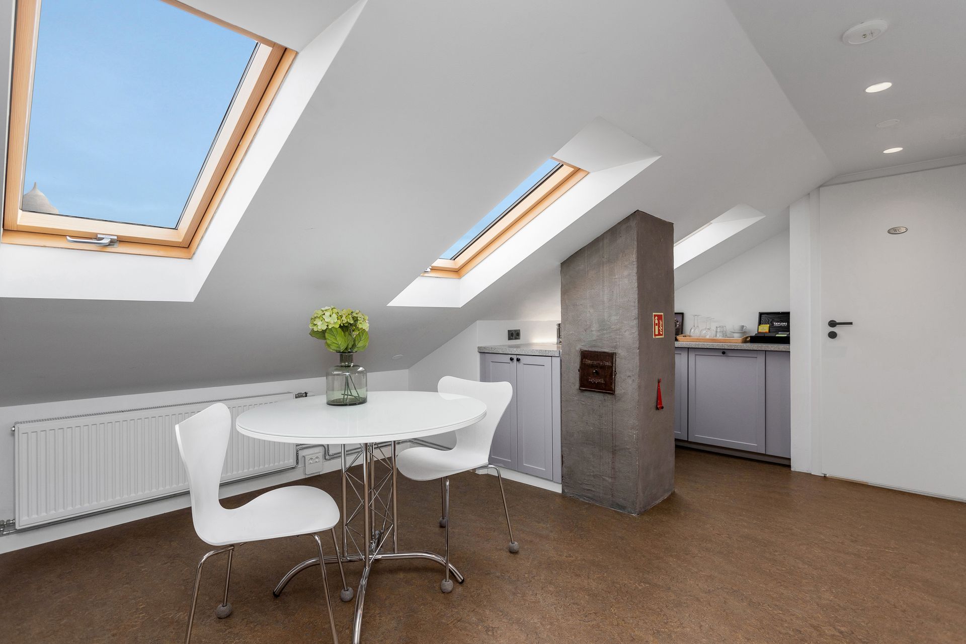 Dining area in attic with skylights, white table and chairs, and kitchenette.
