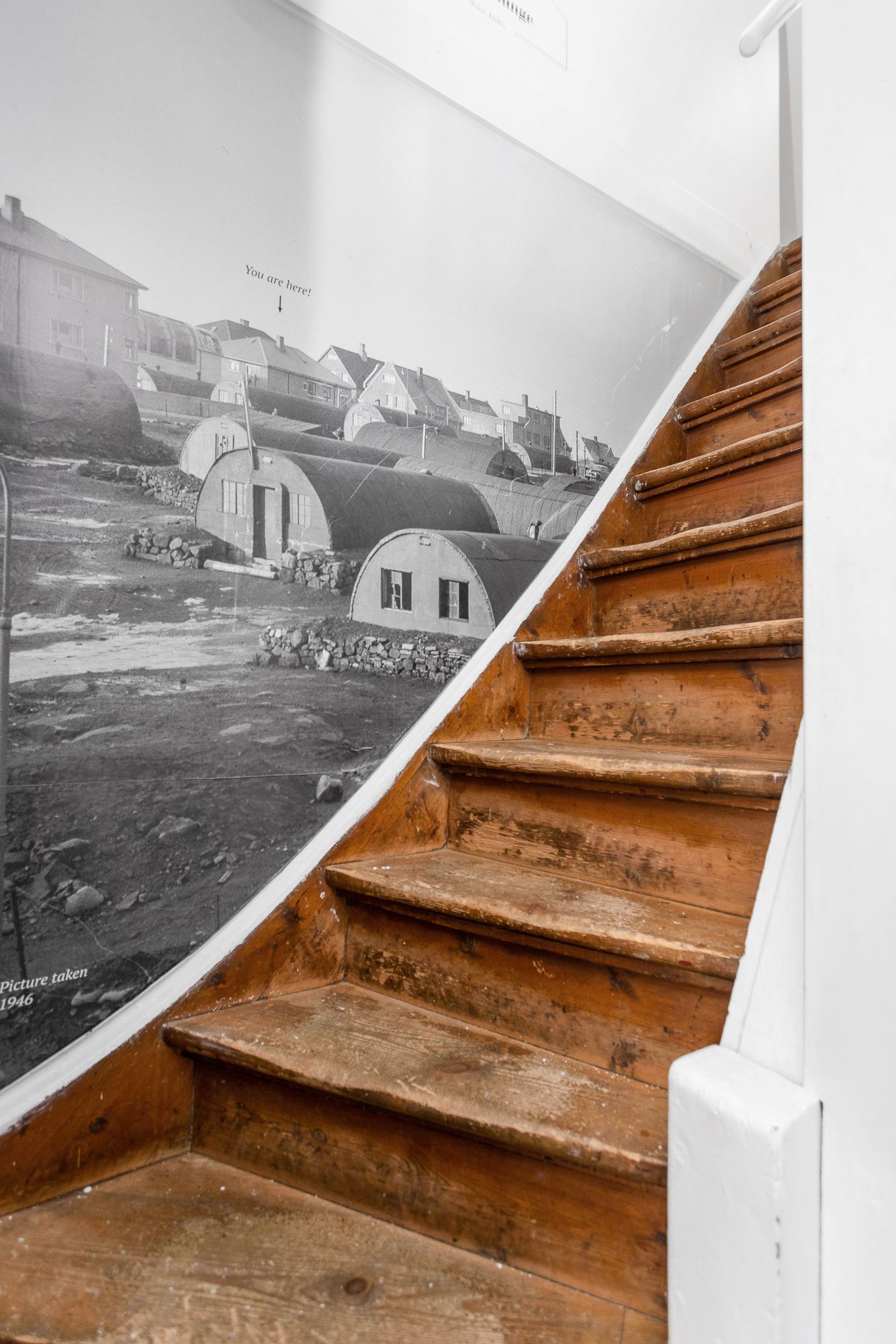 Wooden staircase with a black and white mural of buildings; white walls.