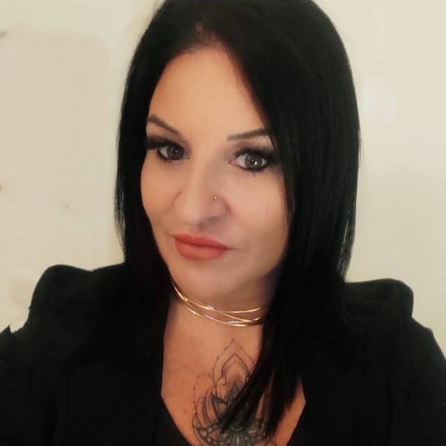 Mujer de cabello y maquillaje oscuro, vestida con un blazer negro y una gargantilla dorada.