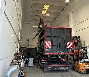 Un camión volquete está estacionado en un almacén al lado de una carretilla elevadora.