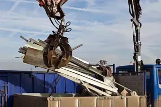 Una grúa está levantando una pila de metal hacia un contenedor de basura.