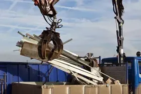 Una grúa está levantando una pila de metal hacia un contenedor de basura.