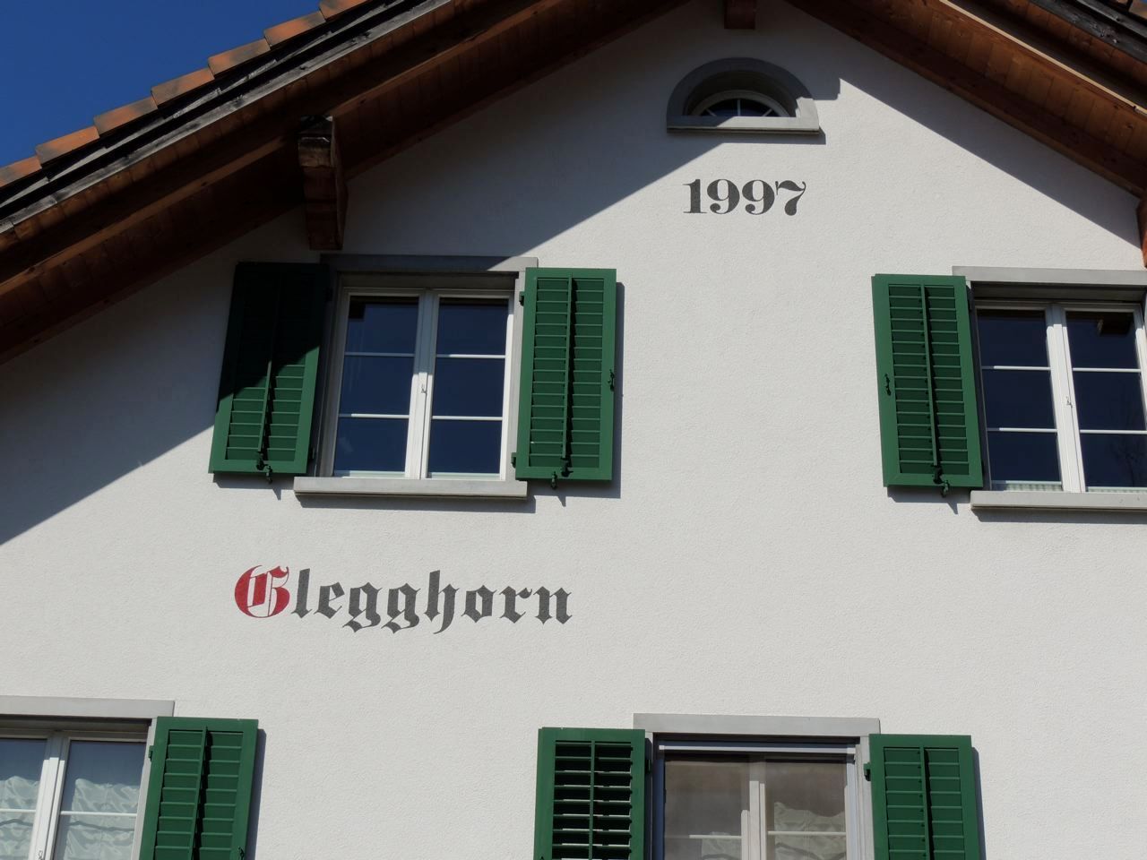 Ein weißes Gebäude mit grünen Fensterläden und der Jahreszahl 1997, Malergeschäft Jost