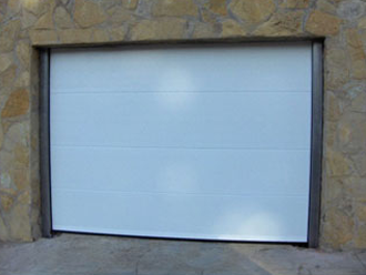 Una puerta de garaje blanca está contra una pared de piedra.