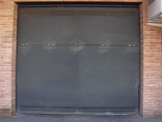 Una pared de ladrillos con una puerta negra delante.