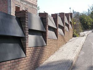 Un muro de ladrillos con una valla negra al costado de una carretera.