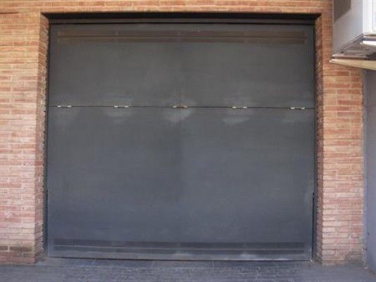 Una puerta de garaje negra con una pared de ladrillos detrás.