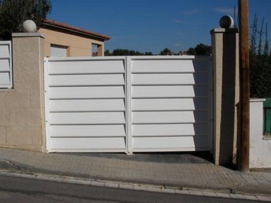 Una puerta blanca está abierta a un camino de entrada frente a una casa.