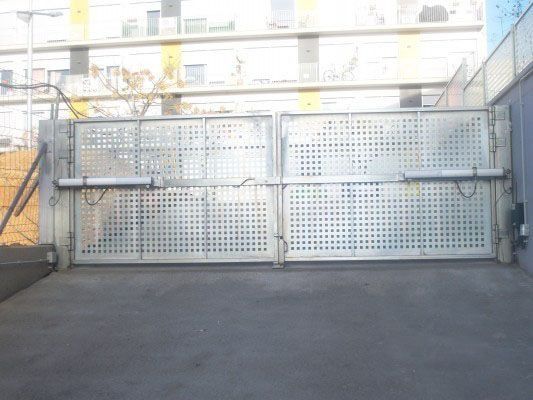 Una puerta de metal con agujeros está cerrada en un estacionamiento.