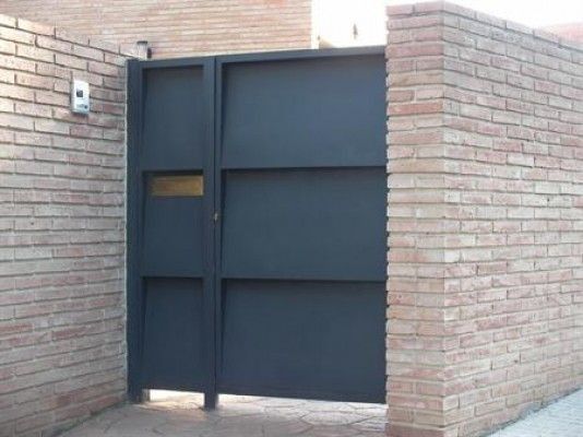 Una pared de ladrillos con una puerta negra delante.