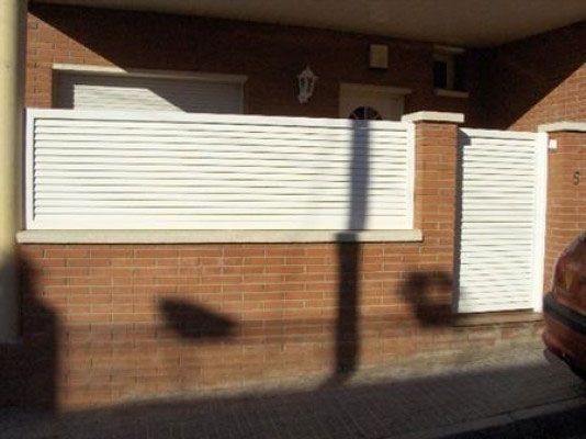 Un coche está aparcado delante de un edificio de ladrillo con una valla blanca.