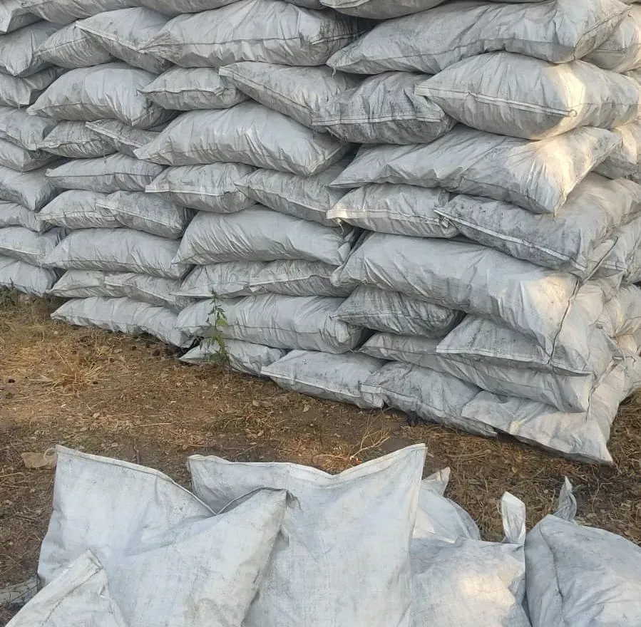 Bolsas grises apiladas llenas de carbón, al aire libre.