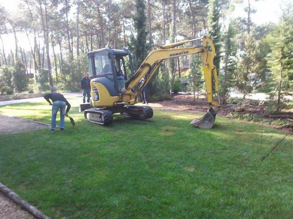 Um homem está cavando na grama ao lado de uma escavadeira amarela