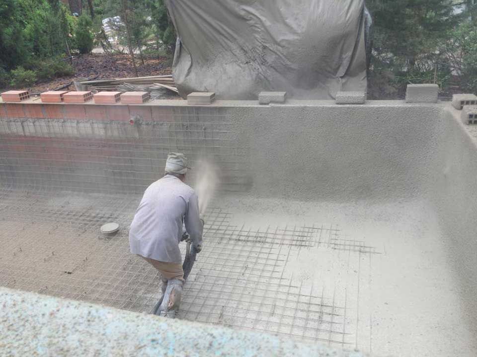Um homem está pulverizando concreto em uma piscina.