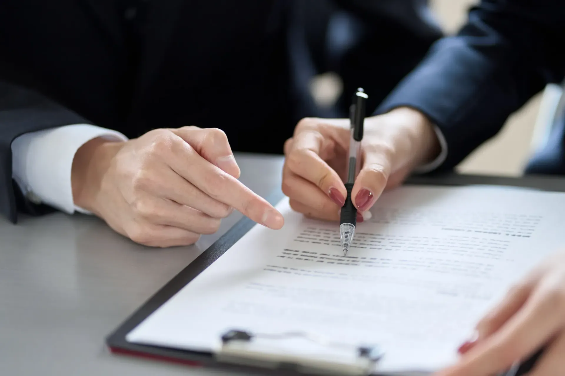 Dos personas de traje revisando y firmando un documento en un portapapeles.