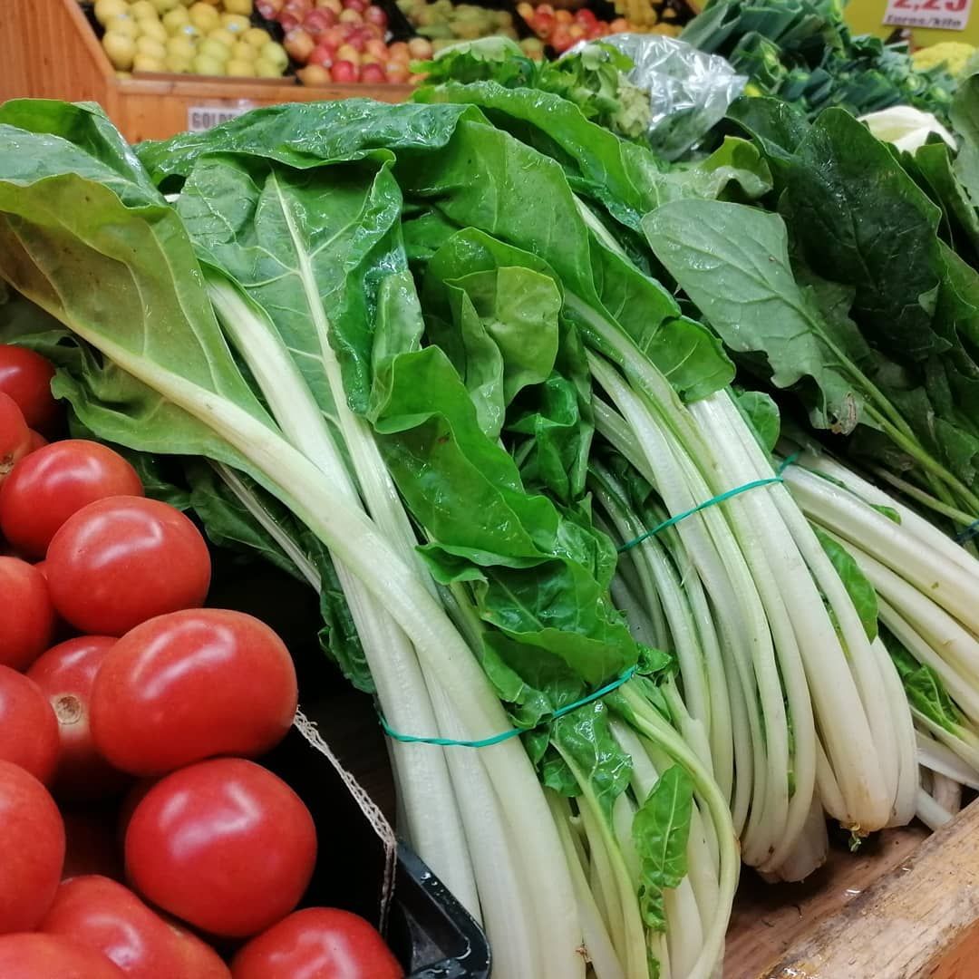 Acelga fresca con tallos blancos y hojas verdes junto a tomates rojos en un supermercado.