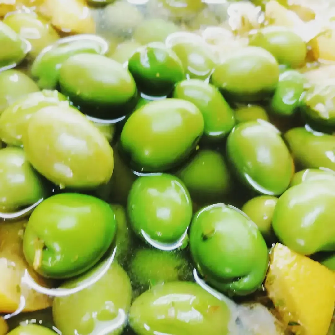 Aceitunas verdes sumergidas en líquido, posiblemente salmuera. Se aprecian algunos trozos amarillos.