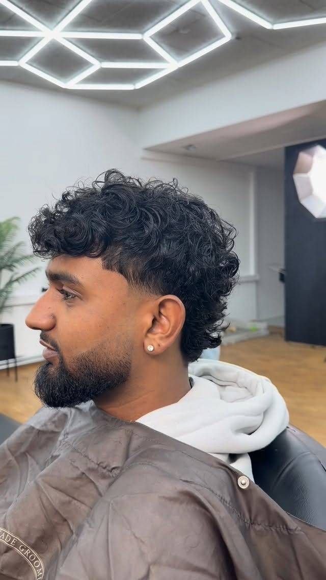 Ein Mann mit lockigem Haar und Bart lässt sich in einem Friseursalon die Haare schneiden.