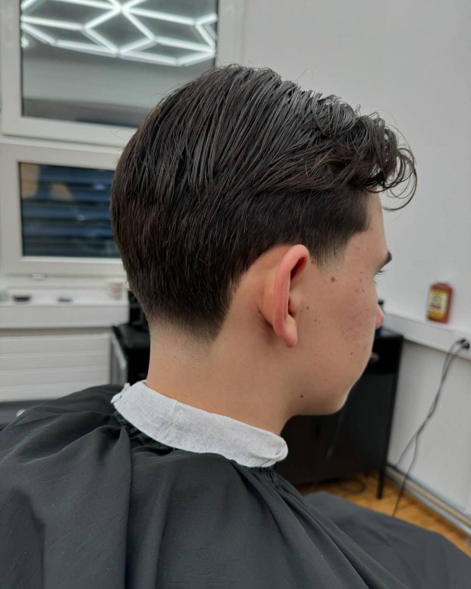 Ein Mann mit dunklem, kurzem Haarschnitt, an den Seiten ausrasiert. Er trägt einen Friseurumhang.