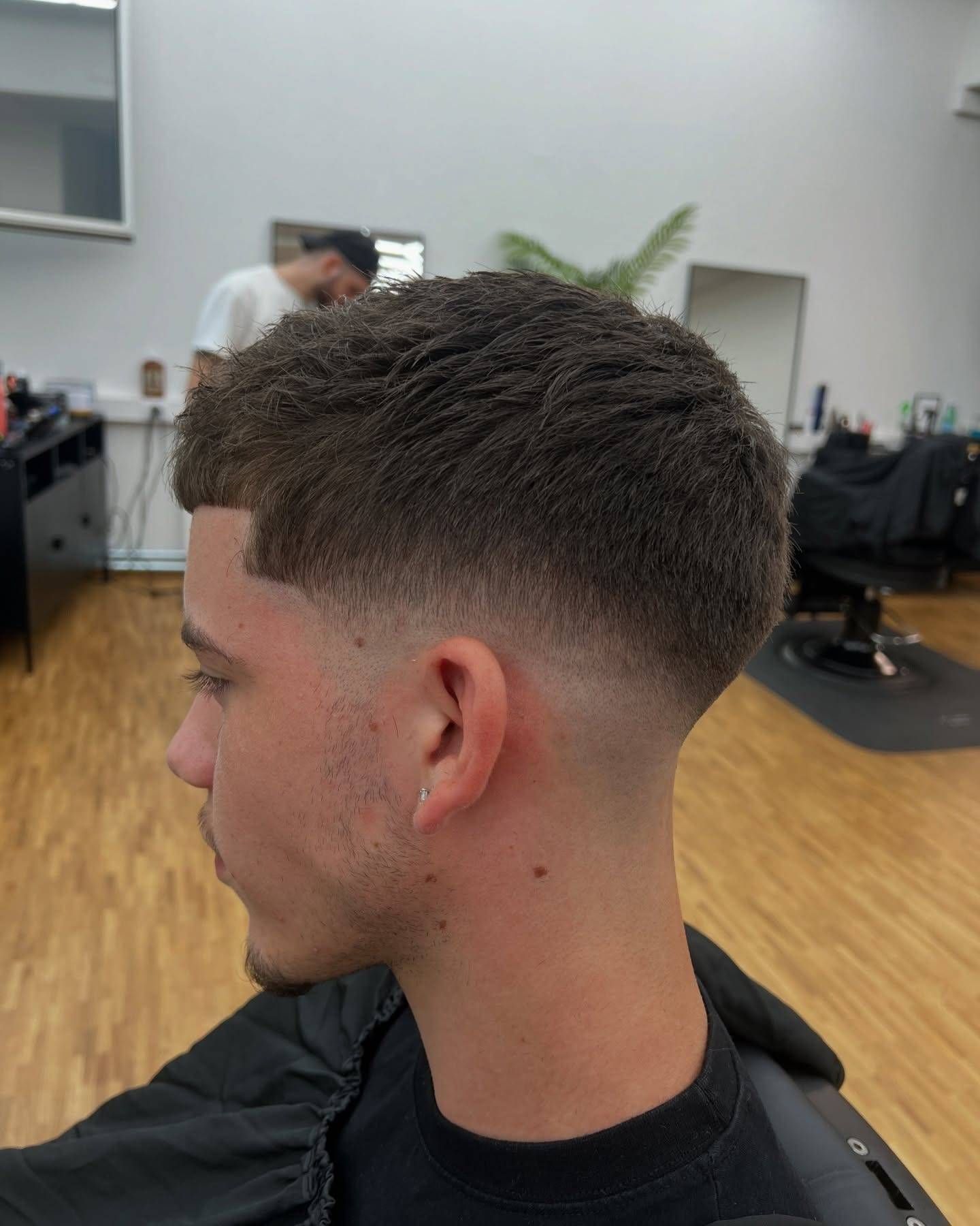 Ein Mann mit einem verblassten Haarschnitt im Friseursalon. Sein Deckhaar ist dunkel und strukturiert, der Übergang sauber.