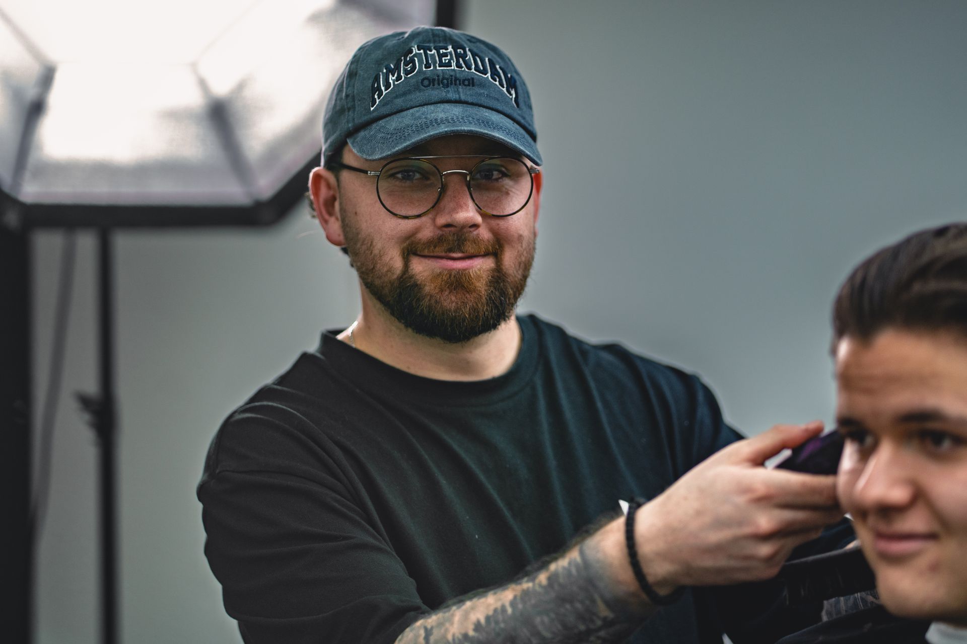 Mann mit Brille und Bart lächelt vor grauem Hintergrund.