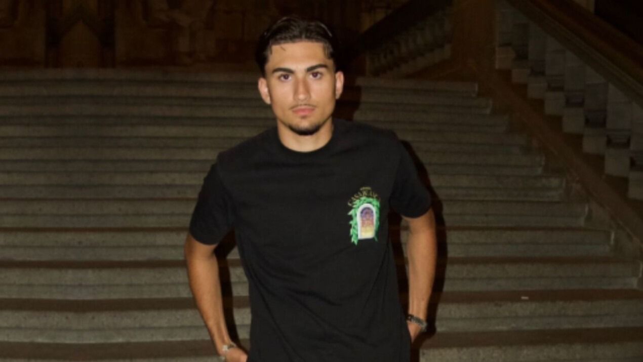 Ein Mann in schwarzem Hemd steht auf einer Treppe und schaut in die Kamera. Nachtszene, beleuchtete Treppe.