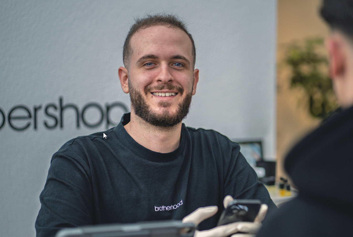 Ein Mann mit kurzem Bart lächelt in die Kamera. Er trägt ein schwarzes Hemd. Im Hintergrund sind ein See und Bäume zu sehen.